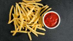 A pile of french fries next to a small bowl of ketchup