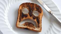A sad face is punched out of a burnt piece of toast.