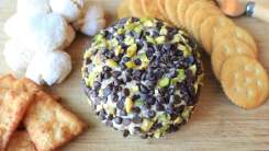 A cheeseball covered in chocolate chips and pistachios on a cutting board with crackers.