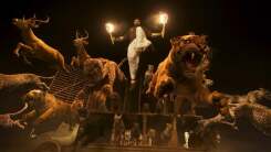 Several wild animals, including tigers, race forward from a pen, lead by a leaping man holding a torch in each hand.