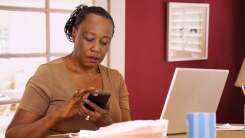 older woman using laptop and smartphone to calculate numbers