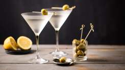 Two martinis in frosted martini glasses sit on a wooden table with olives and a halved lemon.