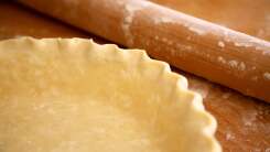 A pie crust next to a rolling pin.