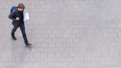 Young man wearing backpack and carrying folders walking across cement path