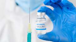 Gloved hand holding Novavax vaccine syringe and bottle 