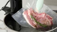 Tongs holding a vacuum-sealed pork chop over a pot of water