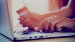 person typing on computer with one hand and holding credit card in the other