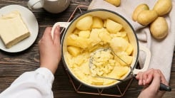 Hands holding potato masher and mashing a pot of potatoes