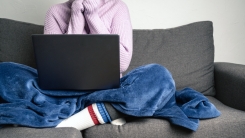 Person wearing sweater and blanket while working on laptop on couch