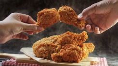 Two hands holding fried chicken over a pile of fried chicken