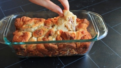 Fingers pulling a piece of cheesy monkey bread from a loaf pan.