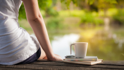 Young woman sitting beside coffee cup and notebooks on rustic wood bench with lake in background