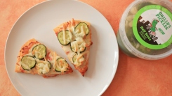 Pickles on two pizza slices on a plate.