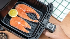 A hand holding an air fryer basket with two raw salmon fillets.