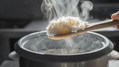 A steaming scoop of rice hovering over a rice cooker.