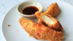 A bitten chicken tender on a plate with two others and soy sauce