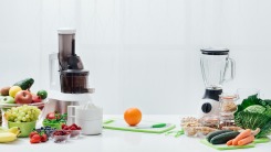 A juicer and a blender on a counter with fruits and veggies
