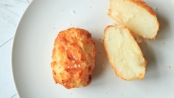 A crispy potato on a plate next to a split crispy potato.