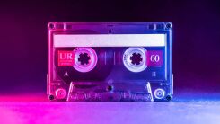 A blank cassette tape standing on end against a smoky pink background
