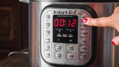 Close-up of a hand pressing a button on the panel of an Instant Pot