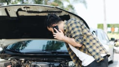 Man looking at car engine while on smartphone