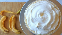 Whipped cream topped pie next to banana peels formed in the shape of pi.