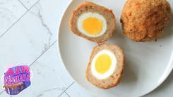 A scotch egg next to another one which has been sliced in half.