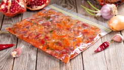 A zip top bag filled with sauce and laying on a table with other ingredients.