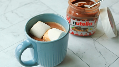 A cup of hot chocolate next to an open jar of Nutella.