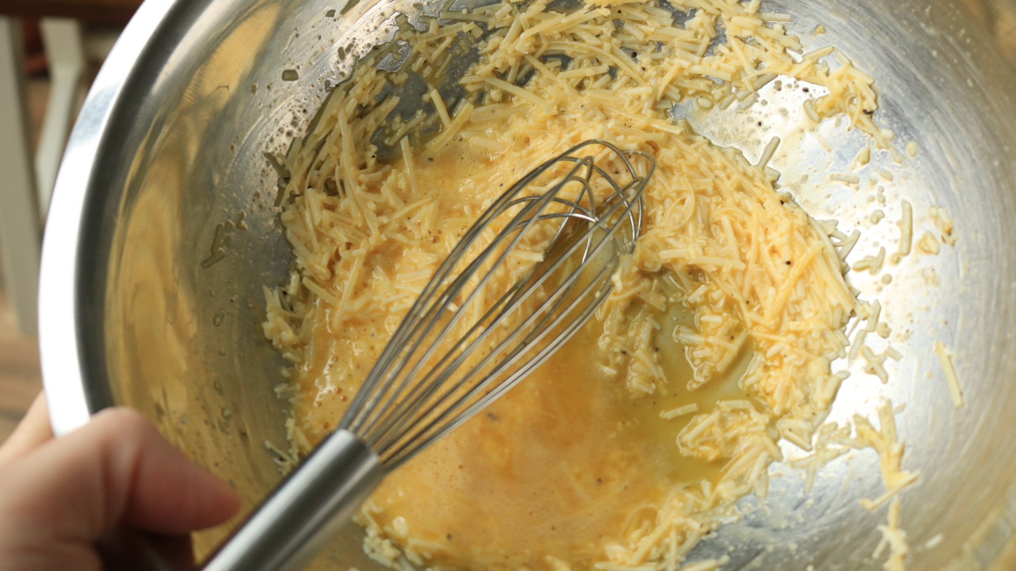 A small whisk in a bowl of eggs and cheese.
