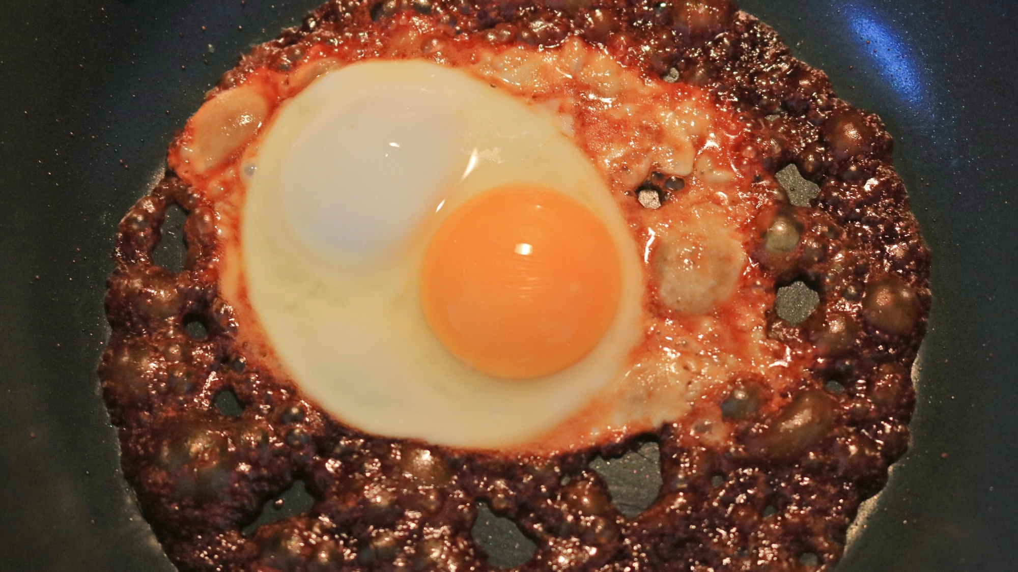 An egg frying in dark sauce in a pan.