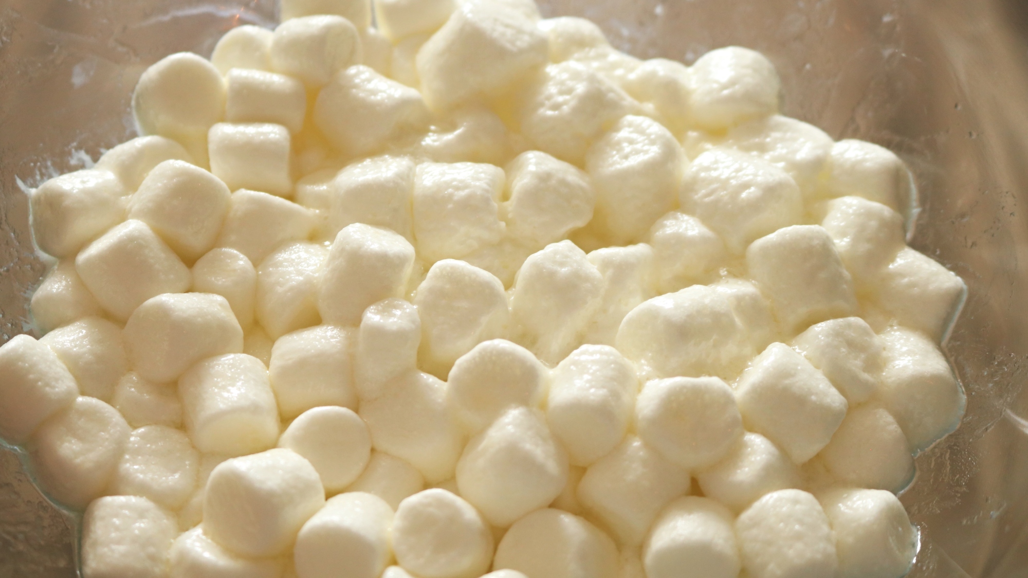 Mini marshmallows tossed with butter in a clear bowl.