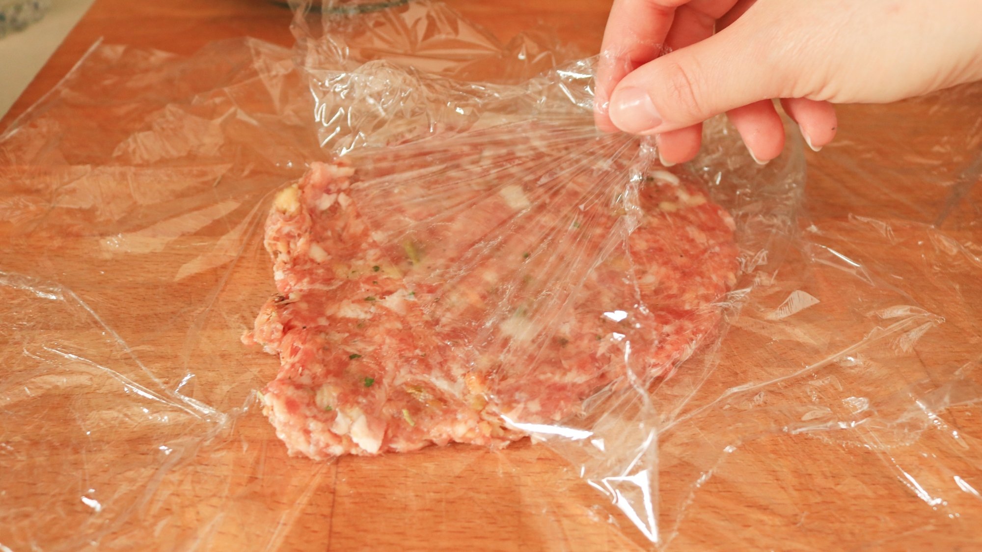 A hand peeling plastic wrap off of a sausage patty.