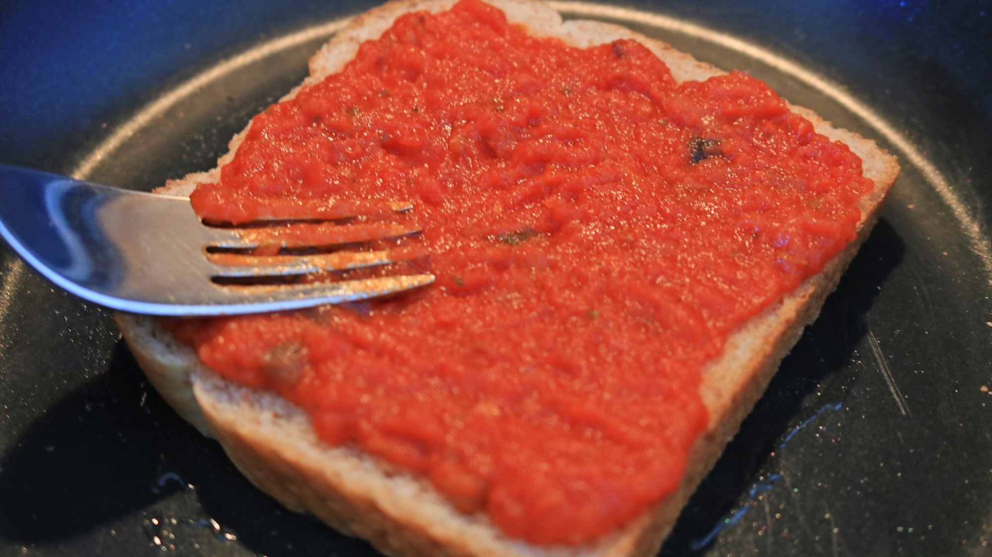 A fork pressing tomato sauce onto a slice of bread.