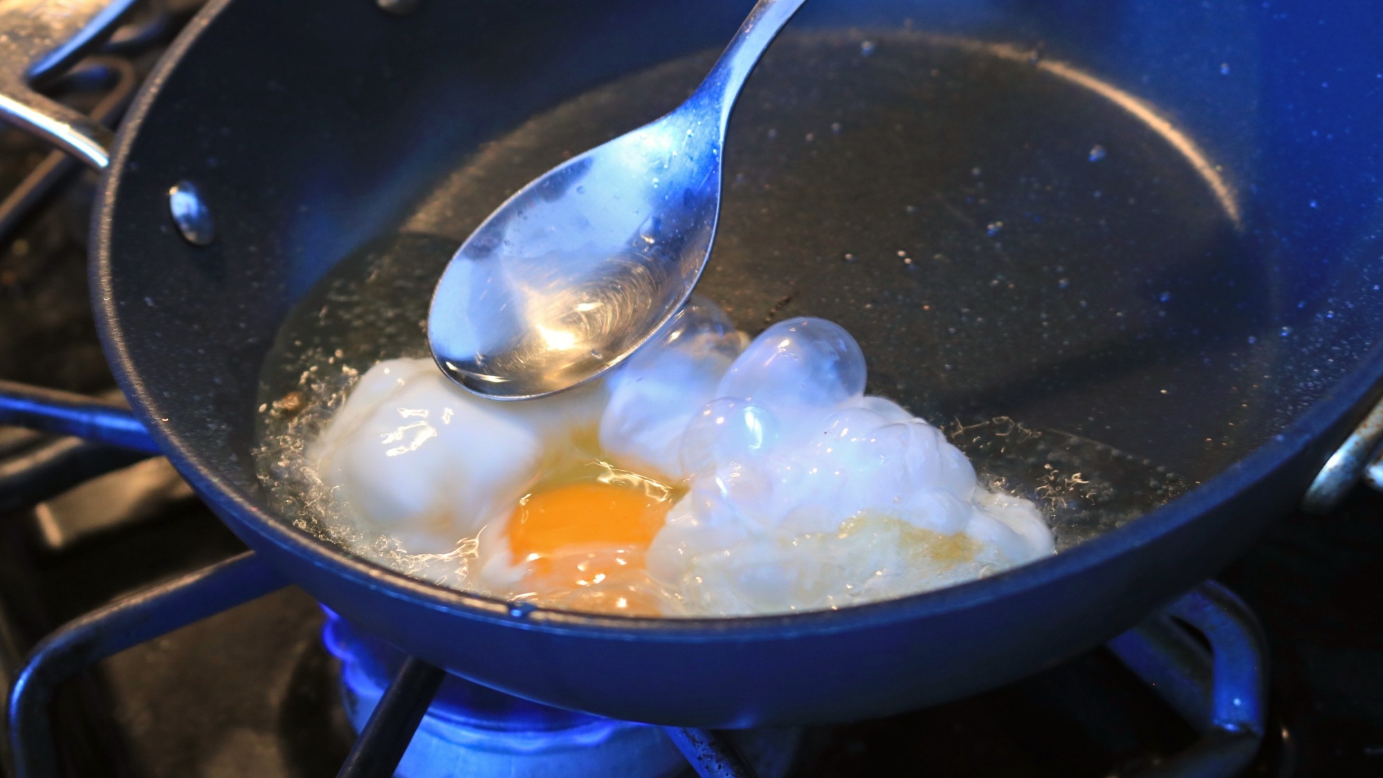 Spoon over an egg bubbling in a pan.