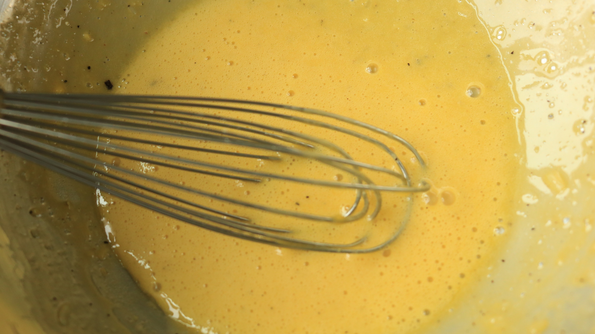 A whisk in a bowl of yellow sauce.
