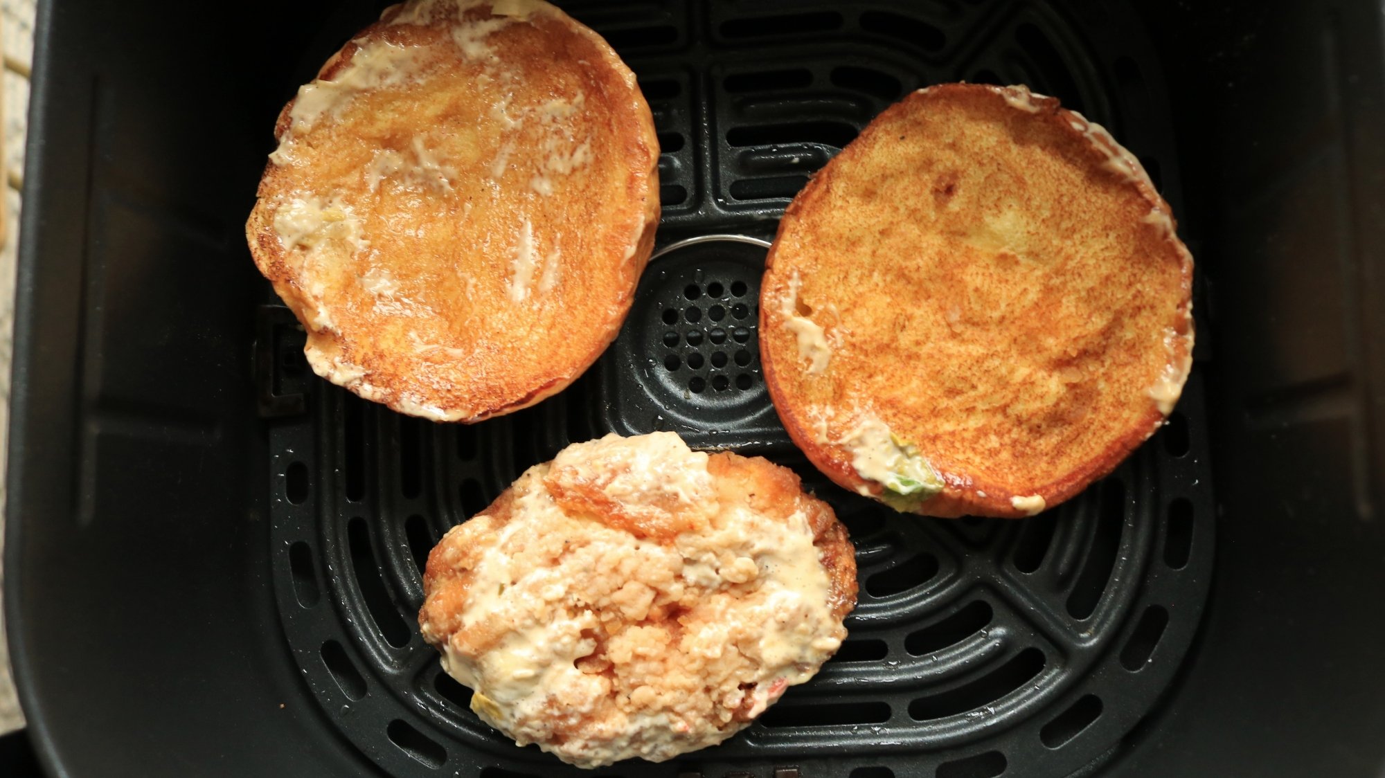 A burger bun and chicken patty in an air fryer basket.