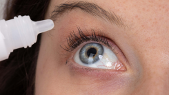 A person holding a bottle of eye drops above their eye