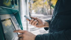 A person at an ATM, holding a phone