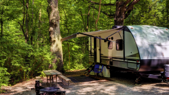 A towable RV trailer in a clearing in the woods.