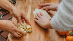 Two pairs of hands arranging cheeses on a wooden board