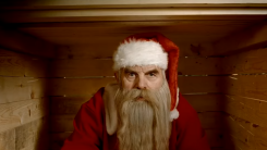 A screenshot of a haggard looking Santa sitting in a fireplace from the film Rare Exports