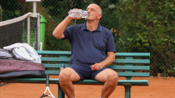 older man sitting on a bench drinking water bottle after playing tennis