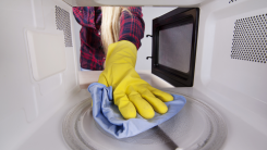 A person's hand reaching into a microwave with a washcloth