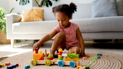 little girl playing alone with blocks and a train on the floor