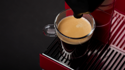 An espresso cup being filled by a red Nespresso coffee maker