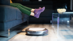 A robot vacuum cleans while someone watches TV