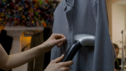 A person steaming a hanging blue button down shirt