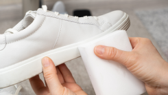 A person cleaning a pair of white sneakers with a melamine sponge