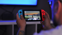 A photograph from an over-the-shoulder perspective of a person playing Legend of Zelda on a Nintendo Switch with blue and red Joy-Con controllers.